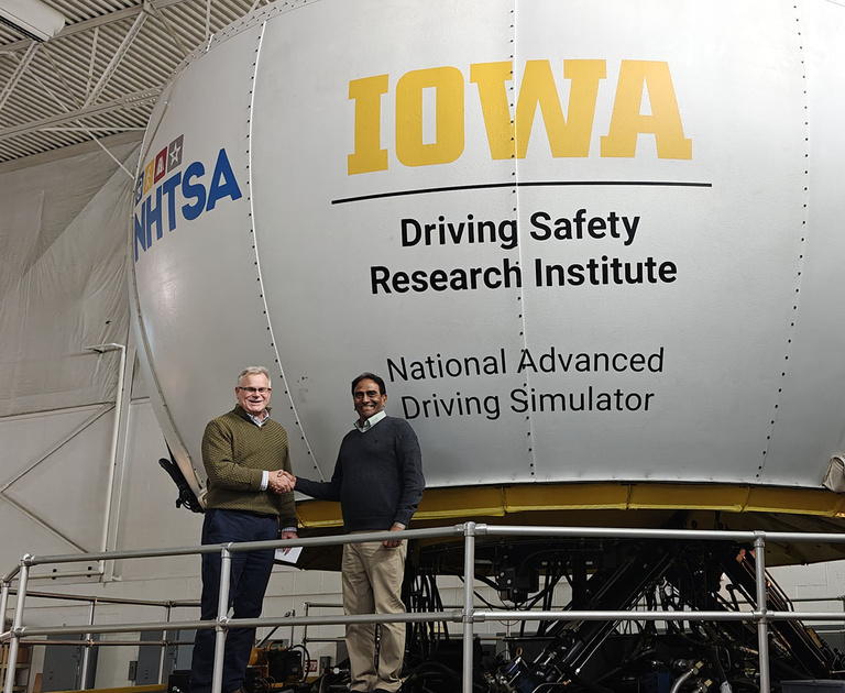Raju Dandu and Dan McGehee shake hands in front of the NADS-1 simulator